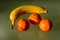 Yellow banana and orange color clementines groupped in closeup view on reflective glass