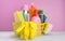 In a yellow basket, on a pink background, a set of items for cleaning, rags, sponges, brushes, liquids for disinfection