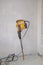 Yellow battered large hammer drill, jackhammer or perforator, for interior work is attached to plastered wall in the interior,