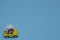 A yellow Beetle with a flower bow on the roof rides on a blue background with copy space. Minimalistic car scene