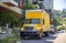 Yellow big rig semi truck delivering cargo in box truck standing on the street parking spot with multilevel buildings