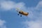 Yellow Biplane Flying in Blue Sky and Clouds