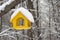Yellow bird feeder with roof covered with snow in winter forest
