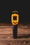 Yellow-black pyrometer on a wooden background. A device for non-contact temperature measurement