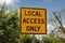 Yellow and black square road sign in neighborhood reading Local Access Only against a blue sky with clouds