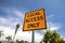 Yellow and black square road sign in neighborhood reading Local Access Only against  a blue sky with palm trees