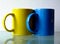Yellow and blue coffee cups in abstract closeup view. reflective glass surface