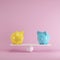 Yellow and blue piggy banks playing with white seesaw on pink background