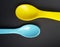 Yellow and blue plastic spoons isolated over black background. Little spoons for feeding babies and toddlers.