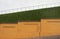 Yellow brick fence against the green grass slope and white wall