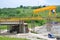 Yellow bridge crane on construction site of slovak D1 highway. Except for the crane there are some workers and cars.