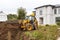 yellow bucket excavator levels pile of earth in front of country cottage