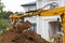 yellow bucket excavator levels pile of earth in front of country cottage