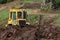 Yellow bulldozer earthworks in a park on background of plants