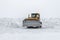 Yellow bulldozer removes snowdrifts in a severe snowstorm at winter