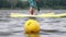 A yellow buoy is floats in a lake, on a background young persons rides on a paddleboard