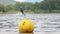 A yellow buoy is floats on a surface in a lake with a surfer