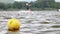 A yellow buoy is floats on a surface in a lake with a surfer