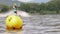 A yellow buoy is floats on a surface in a lake with a surfer