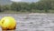 A yellow buoy is floats on a surface in a lake with a surfer