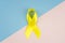 Yellow cancer awareness ribbon as symbol of childhood cancer awareness on blue and pink background. Copy space
