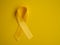 Yellow cancer awareness ribbon on a yellow background. Top view Childhood Cancer Awareness day flat lay