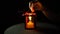 A yellow candle burns in a metallic red lantern on a black background, close-up.