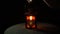 A yellow candle burns in a metallic red lantern on a black background, close-up.