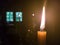 A yellow candle with a long flame in the altar of an Orthodox church near the throne with a menorah opposite the window