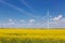 In the yellow canola field stands a white turbogenerator, against the sky with clouds, the concept