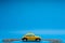 Yellow car figurine surrounded by a bunch of coins, on blue background