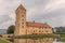 Yellow castle with a tall tower that is reflected in the moat