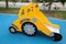 A yellow children`s slide in the form of a tractor with beautiful gears and wheels on a background of blue soft coating.