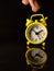 A yellow clock with someone hand with reflection on a black background.