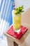 Yellow cocktail with soda bubble topping with mint leaves and slice of lime with red and with strip straw on red napkin