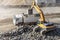 Yellow color excavator is loading some rocks to white color earth dump truck in the construction site.