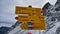 Yellow colored signpost showing hiking duration and directions to different destinations with snow-covered mountains.