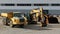 Yellow construction machineries in a row outside the site. A dump truck, an excavator and a bulldozer.