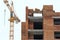Yellow construction tower crane and unfinished brick multistory building