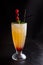 Yellow cooling drink in a tall glass goblet on the black background