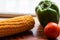 Yellow corn stalk with tomato and capsicum close up photo in wooden background