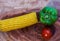 Yellow corn stalk with tomato and capsicum close up photo in wooden background