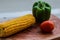 Yellow corn stalk with tomato and capsicum close up photo in wooden background