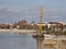 A yellow crane on a barge is standing on the Kuban river pier near the Krasnodar city embankment.