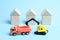 A yellow crawler excavator loads an orange dump truck against the background of houses built from wooden children`s