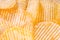Yellow crispy ridged potato chips close up. Food background