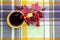 A yellow cup of tea stands on a plaid. Near a mug are clusters of mountain ash, rosehip berries and red autumn leaves. View from