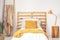 Yellow cushions on wooden bed with blanket in bedroom interior with lamp, plant and ladder. Real photo