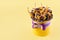 Yellow cylindrical box with a lilac bow filled with dried fruits on a yellow background, copy space