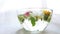 Yellow dandelions, white blooming flowers, green leaves in a glass bowl of water on a sunny table